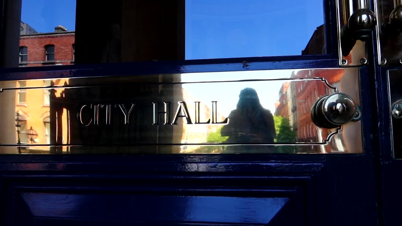 Shiny City Hall nameplate reflecting Dublin street buildings and blue sky