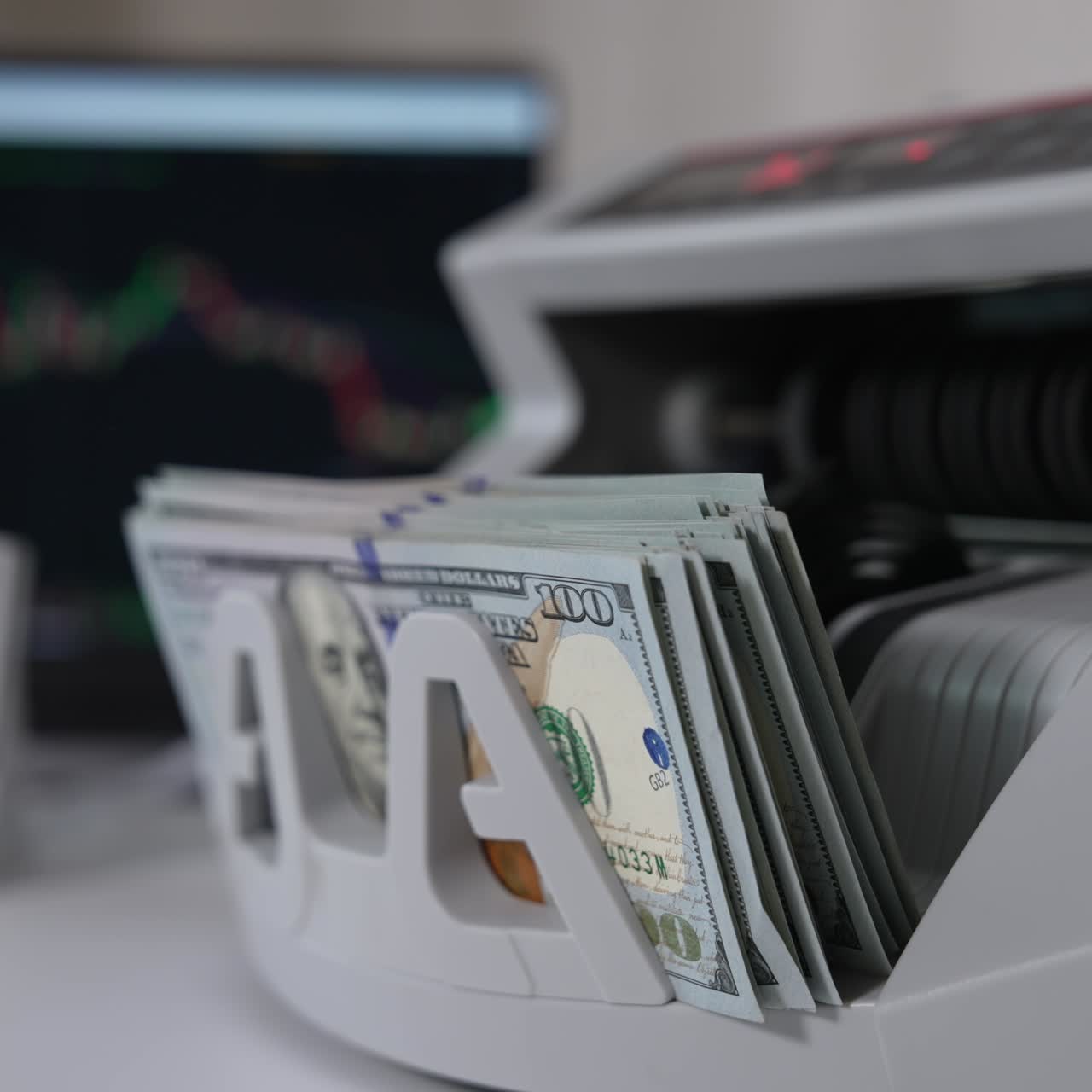 Accensione di una macchina conta soldi per contare una mazzetta di banconote da cento dollari. Primo piano. Laptop sullo sfondo sfocato