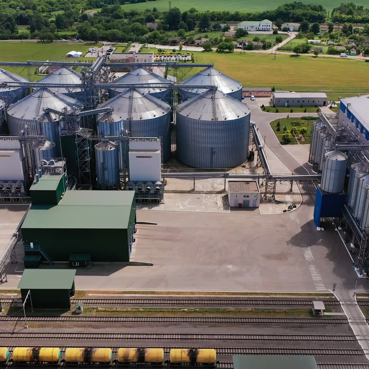 Well-kept industrial plant territory. Large modern agro company for keeping and processing grain from aerial perspective. Village and farmlands at the background