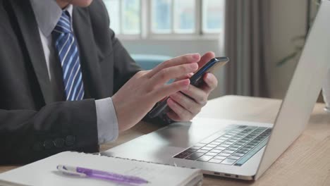 close up of asian businessman wearing business suit using mobile phone after using computer for working at home.