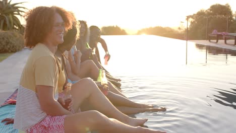 happy diverse friends with drinks talking at pool in slow motion