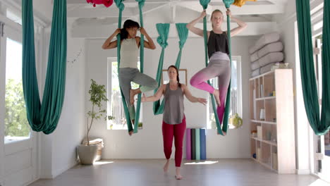 focused diverse fitness teenage girls in aerial yoga class in big white room, slow motion