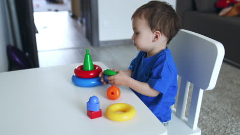 small toddler boy turning colorful toys in hands. lovely kid sits peacefully at desk in his room.