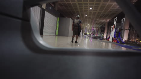 Un-Joven-Mochilero-Caucásico-Viaja-Caminando-Solo-A-Primera-Hora-De-La-Mañana-Usando-Una-Máscara-Protectora-Dentro-Del-Aeropuerto-Llegando-A-La-Puerta-De-Embarque-En-El-Avión