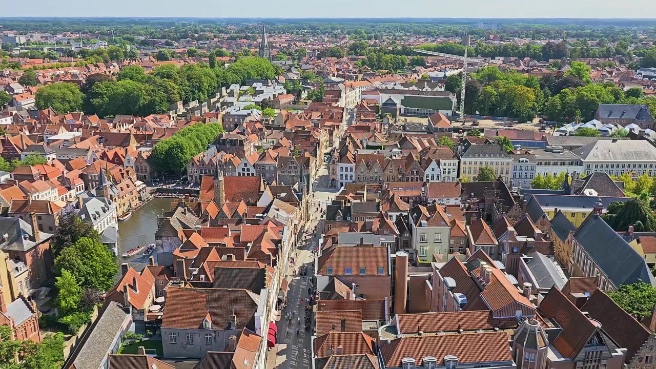 Veduta aerea del centro storico di Bruges, Belgio, con tetti medievali, campanile, edifici colorati, strade strette, parchi e campagna distante sotto un limpido cielo estivo, scena di viaggio