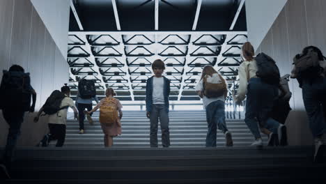 students running upstairs ignoring upset boy on way. sad guy posing on stairway.