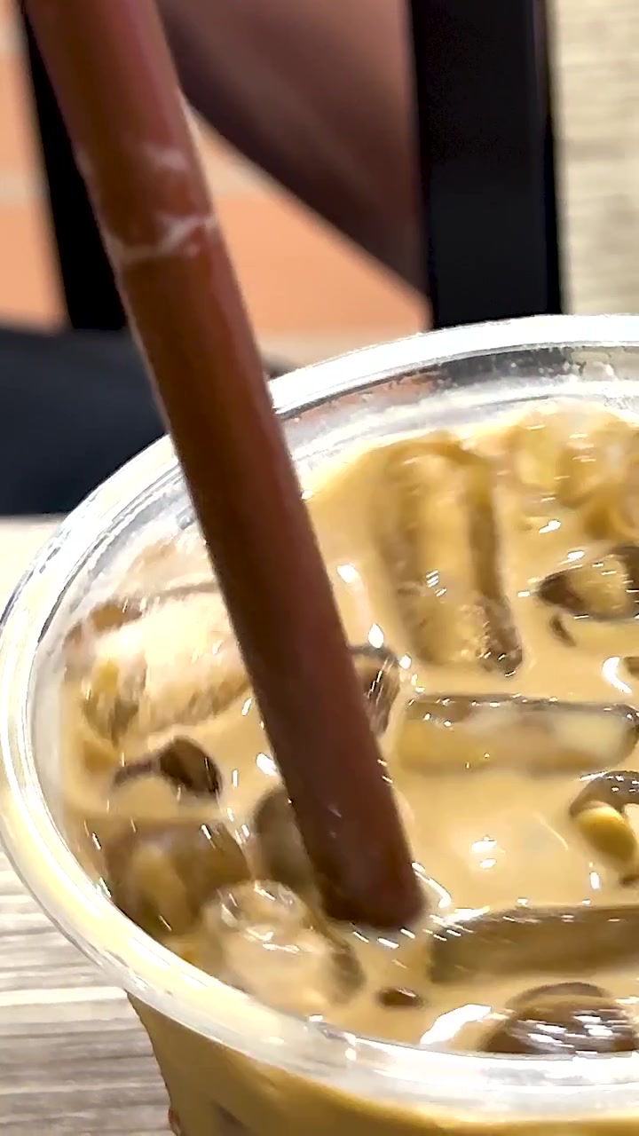 Mano che mescola caffè freddo con una cannuccia