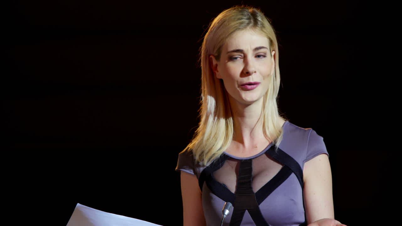 젊은 금발 백인 사업가 여성이 오디토리움 4k에서 비즈니스 세미나에서 연설하고 있습니다.