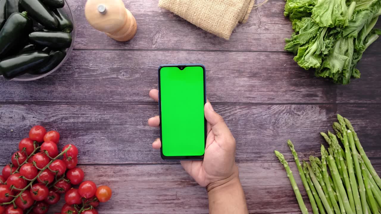 teléfono inteligente con pantalla verde en una mesa de madera rodeado de verduras frescas