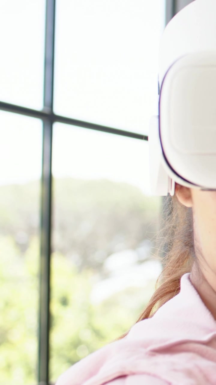 Video verticale: Avvio della VR, donna con top rosa che gira la testa a destra vicino alla finestra, visore VR, spazio per il testo.