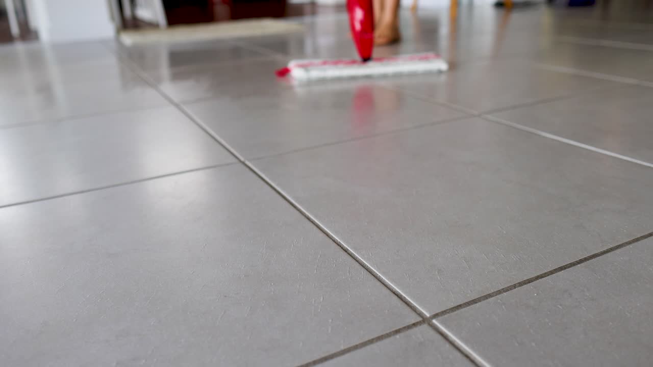 En moppe glider hen over et flisegulv og sprøjter vand i slowmotion, hvilket fremhæver rengøringsarbejdet og teknikken.