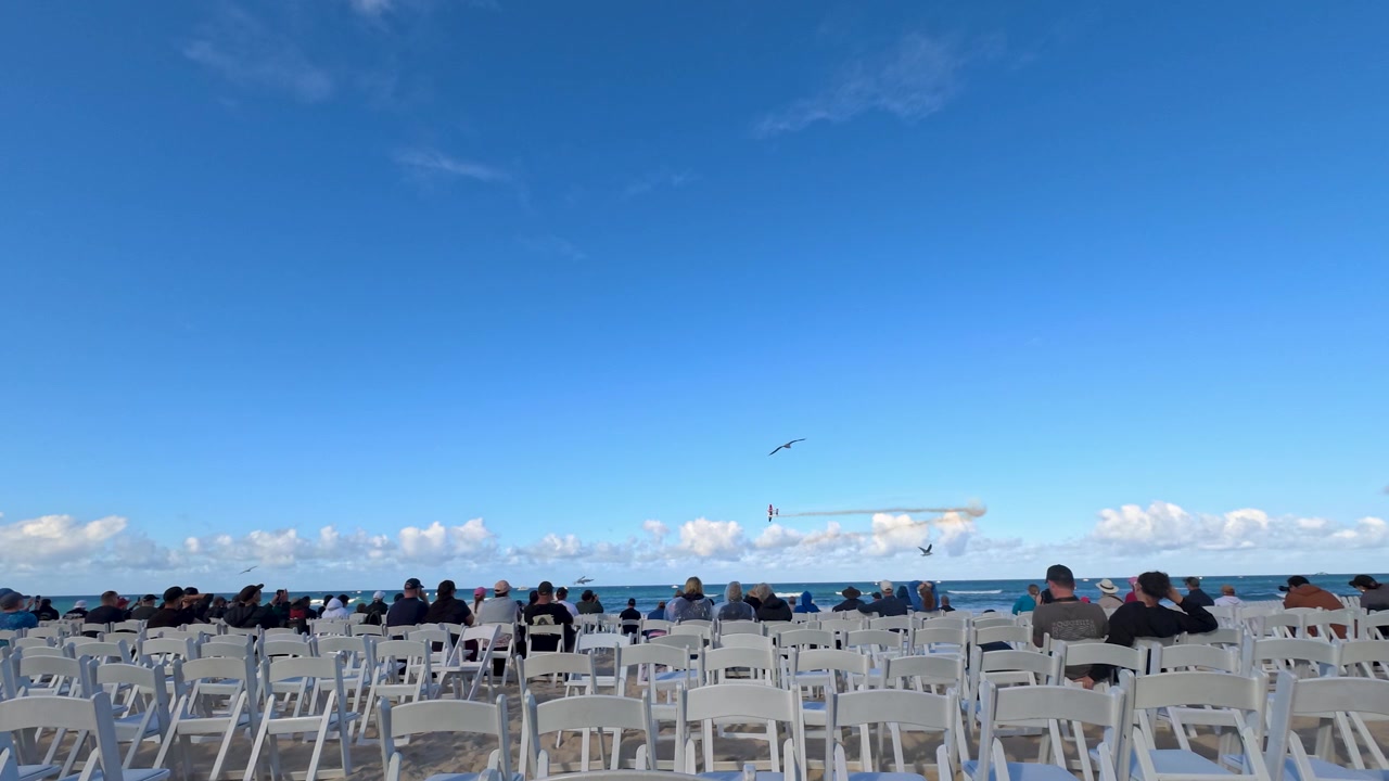 Crowds seated in white chairs watch airplanes perform over the ocean at Surfers Paradise.