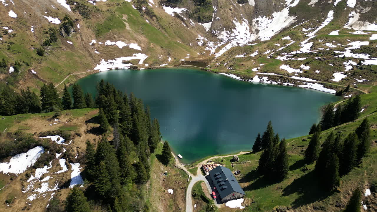 Aerial: Lake Lioson during the day with restaurant and snow in Ormont-Dessous, near Les Mosses, in the canton of Vaud, Switzerland, orbit drone shot