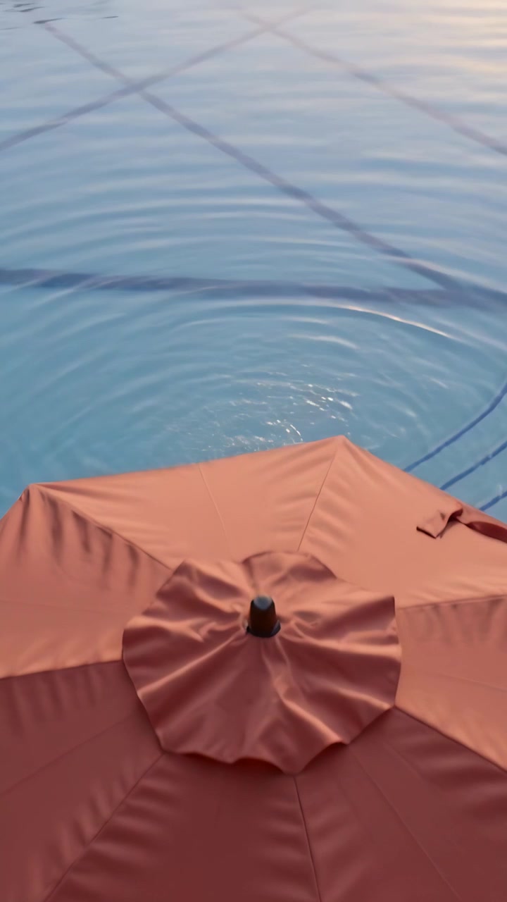 Vertical video: Rippling pool surface causing camera tilt to show red umbrella, pool reflections