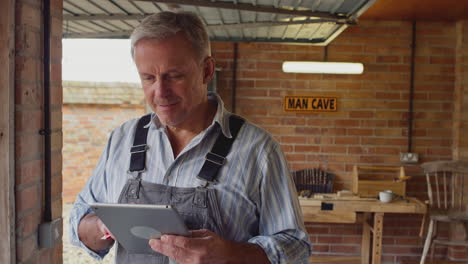 mature male wearing overalls using digital tablet in garage workshop