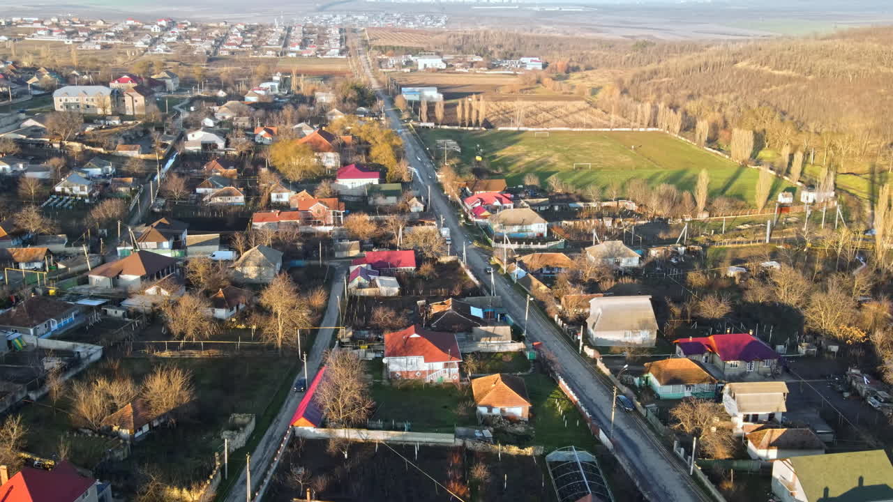 Aerial drone view of a village. View of multiple residential buildings, country roads, bare trees and football field. Sunny weather. Moldova