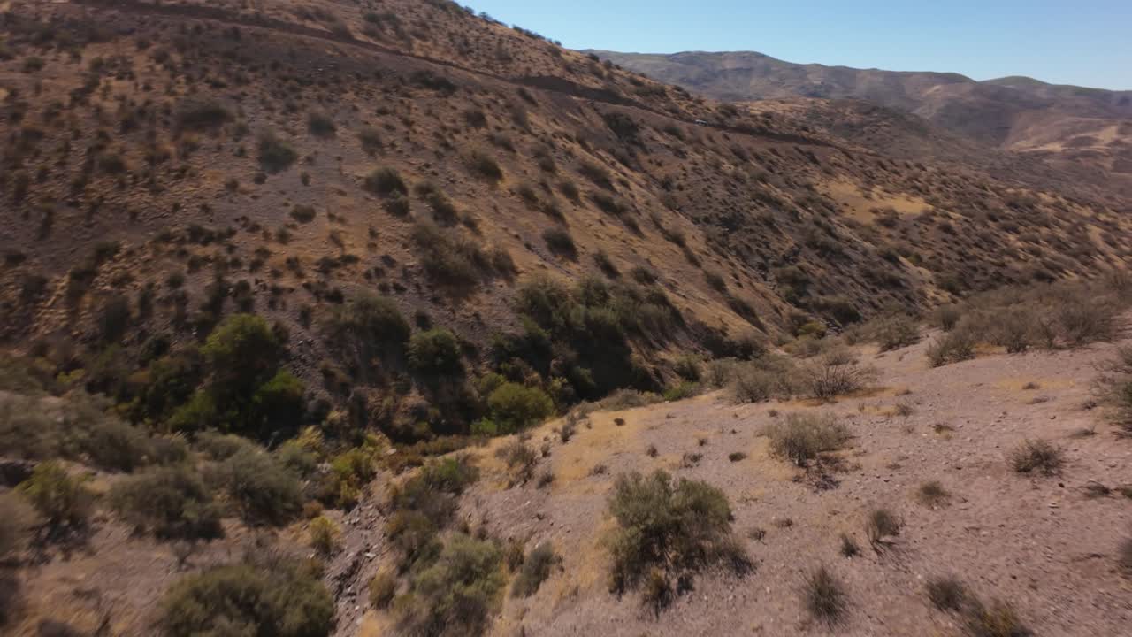 Drone view of dry, rugged hills in northern Chile, with scattered vegetation and deep ravines. Great for geography, travel, or desert-themed visuals.