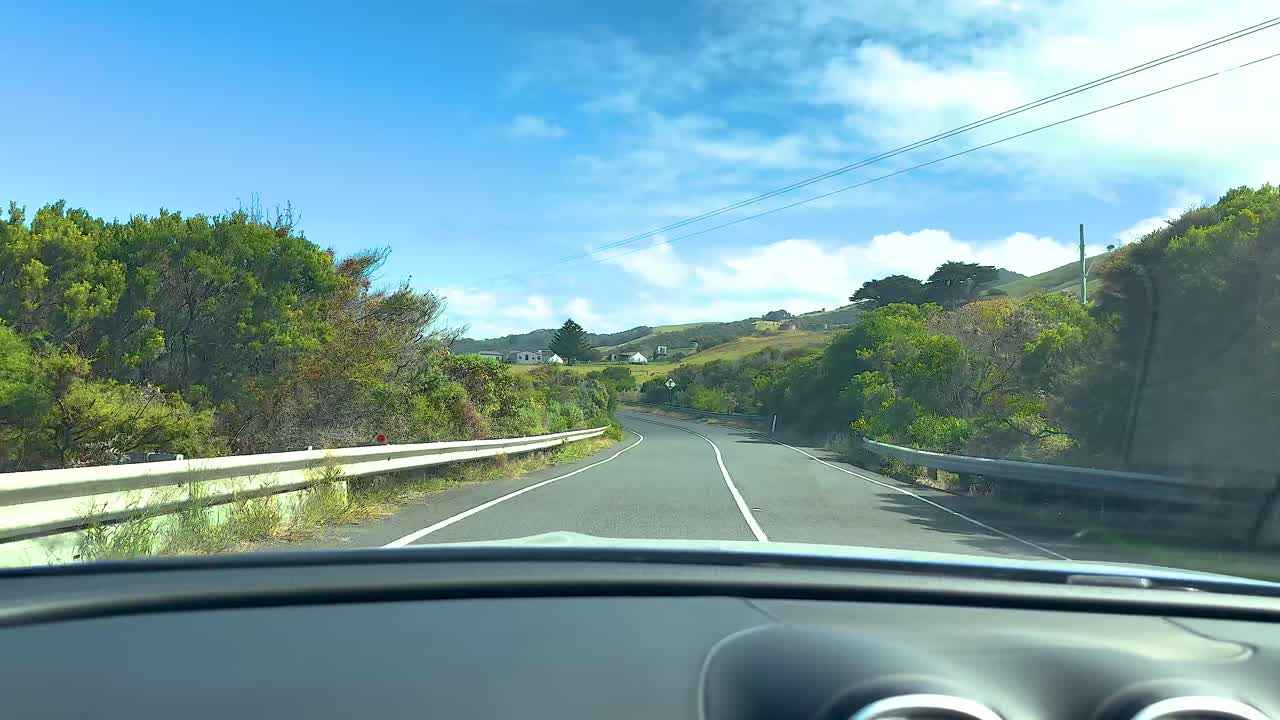 A car journey on a sunny day along the winding Great Ocean Road, surrounded by lush greenery and clear blue skies
