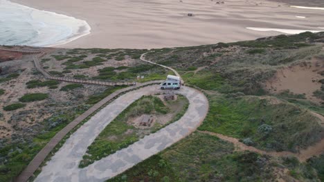 Aerial-view-orbiting-campervan-parked-on-Bordeira,-Portugal-coastline-overlooking-sandy-beach-and-ocean-waves