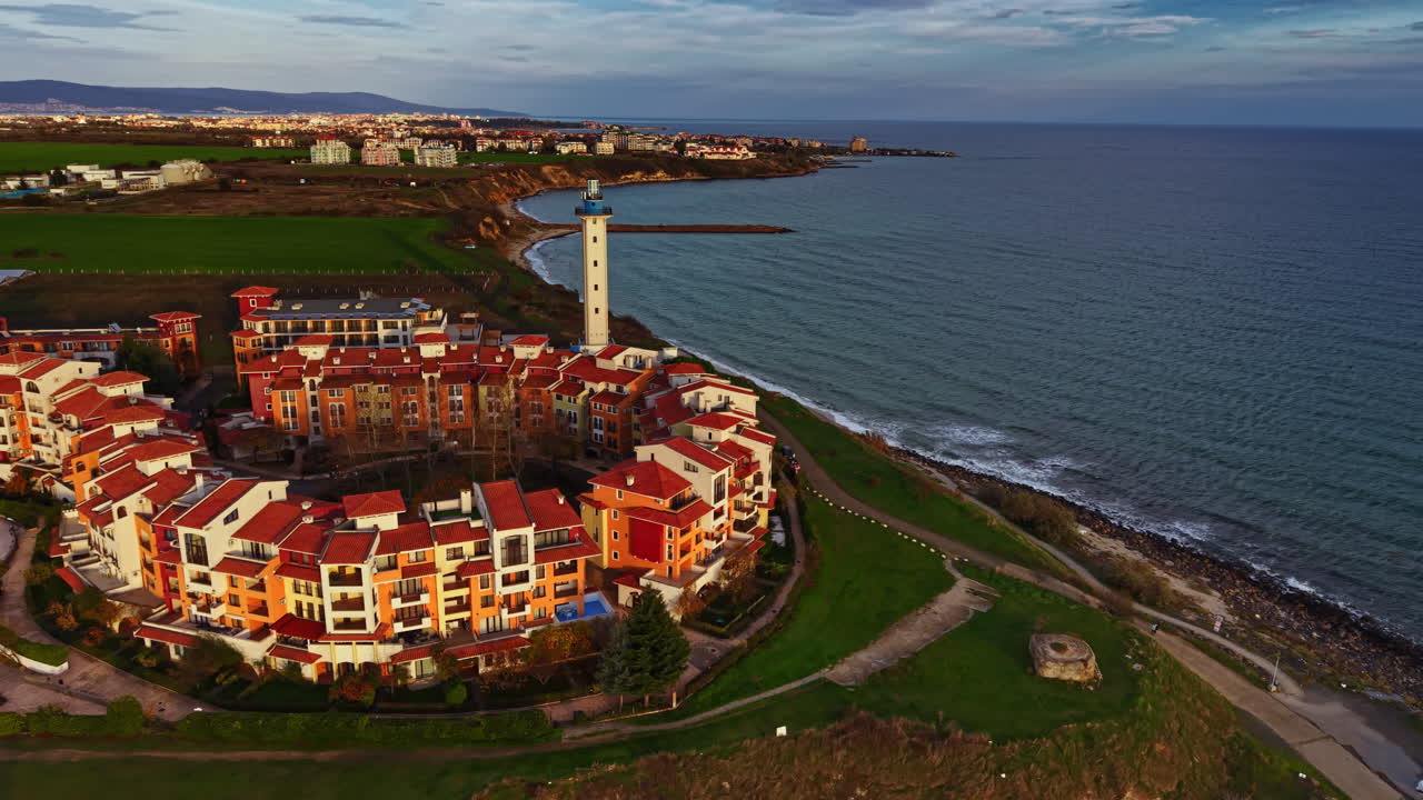 Vista costiera pittoresca che ritrae un incantevole villaggio con tetti rossi, un faro e un mare sereno sotto un cielo rilassante al tramonto