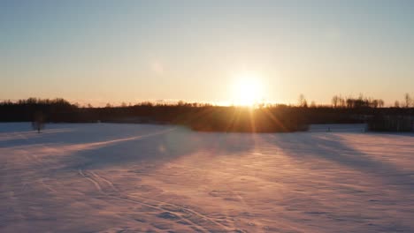 Aerial-view-of-bright-winter-sunset-above-forest-silhouette-and-snowy-field