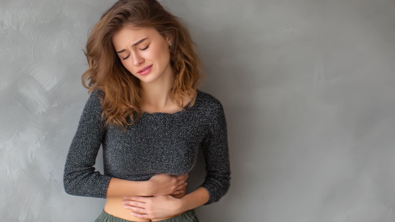 Una giovane donna con un'espressione sofferente che si tiene lo stomaco, esprimendo disagio in un ambiente dai toni di grigio delicati, ritraendo un momento di vulnerabilità e profondità emotiva