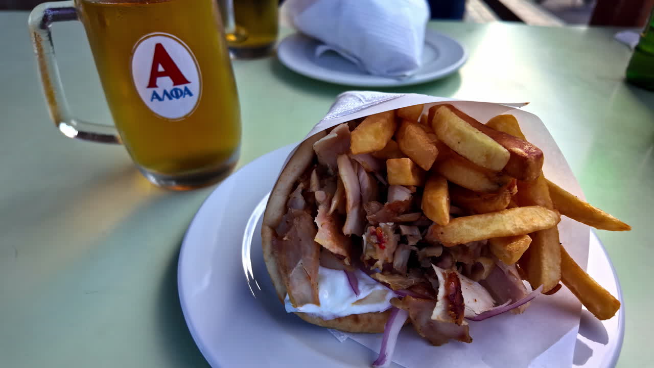 Close-up of a Greek gyro served on a white plate with glass of beer