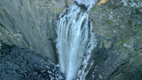 vista de arriba hacia abajo de la cascada en cascada sobre el acantilado escarpado helado a la playa de piedra oscura congelada debajo