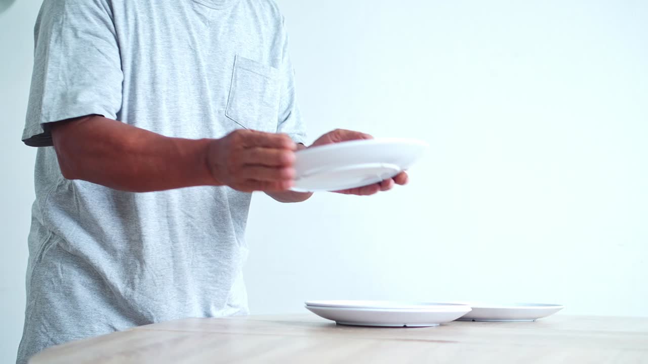 Hands elderly man carefully arranging clean white plates on a smooth wooden table for dining