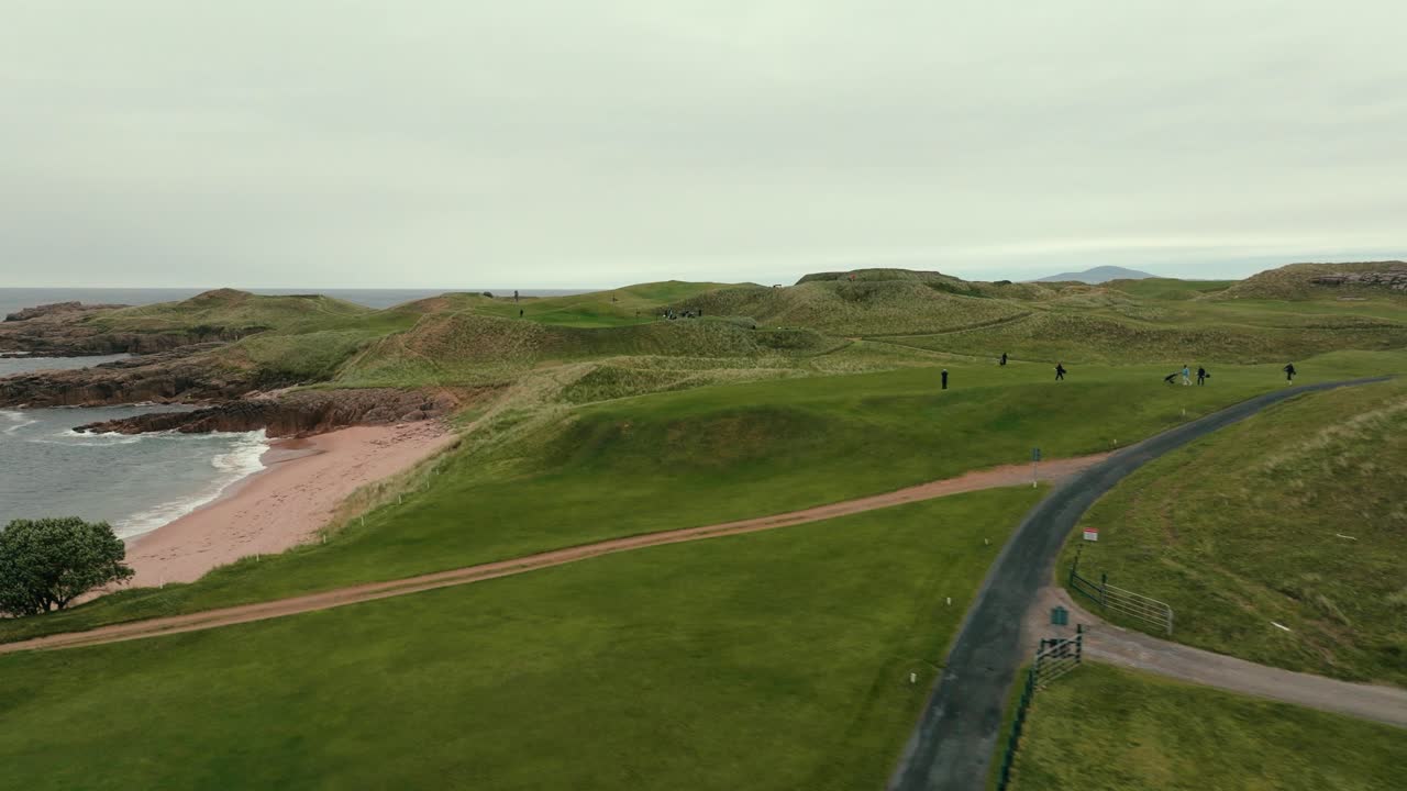 드론이 아일랜드 해안선을 날아다니며 골프 코스를 연결하여 골퍼들이 녹색 페어웨이를 고 있는 것을 보여줍니다.