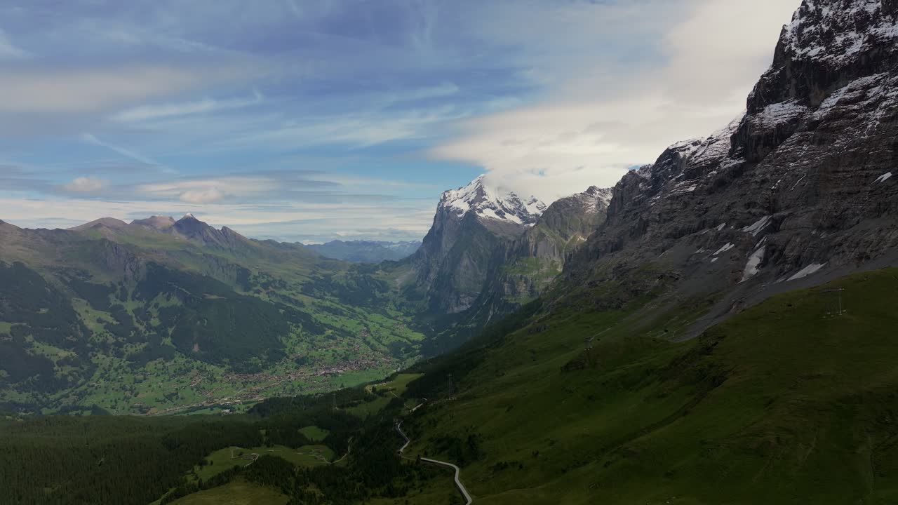 Aerial view of Grindelwald Valley in the Swiss Alps, showcasing lush green meadows, alpine villages, and dramatic cliffs with the snow-capped Eiger mountain towering above