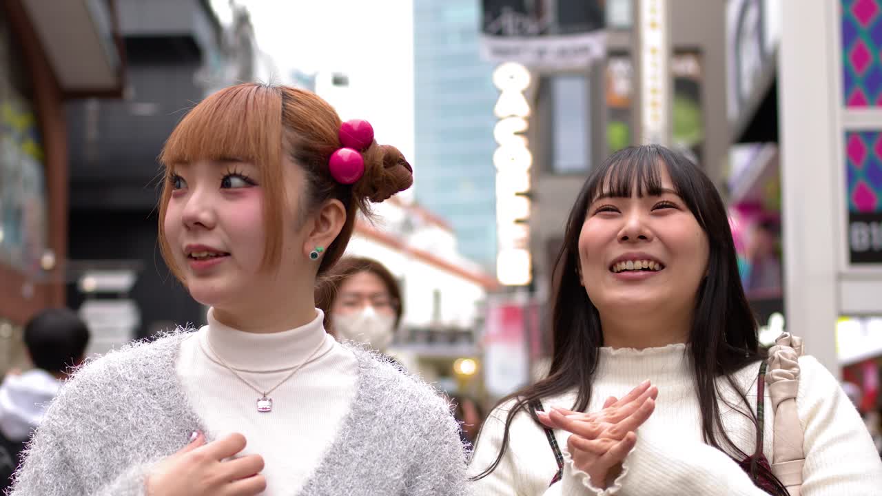 Due giovani donne alla moda parlano e ridono mentre camminano per un affollato quartiere dello shopping di Tokyo