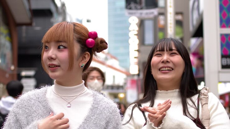 Due giovani donne alla moda parlano e ridono mentre camminano per un affollato quartiere dello shopping di Tokyo