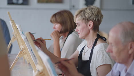 Side-view-of-a-happy-senior-people-smiling-while-drawing-as-a-recreational-activity-or-therapy-in-paint-class-together-with-the-group-of-retired-women-and-men