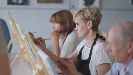 side view of a happy senior people smiling while drawing as a recreational activity or therapy in paint class together with the group of retired women and men