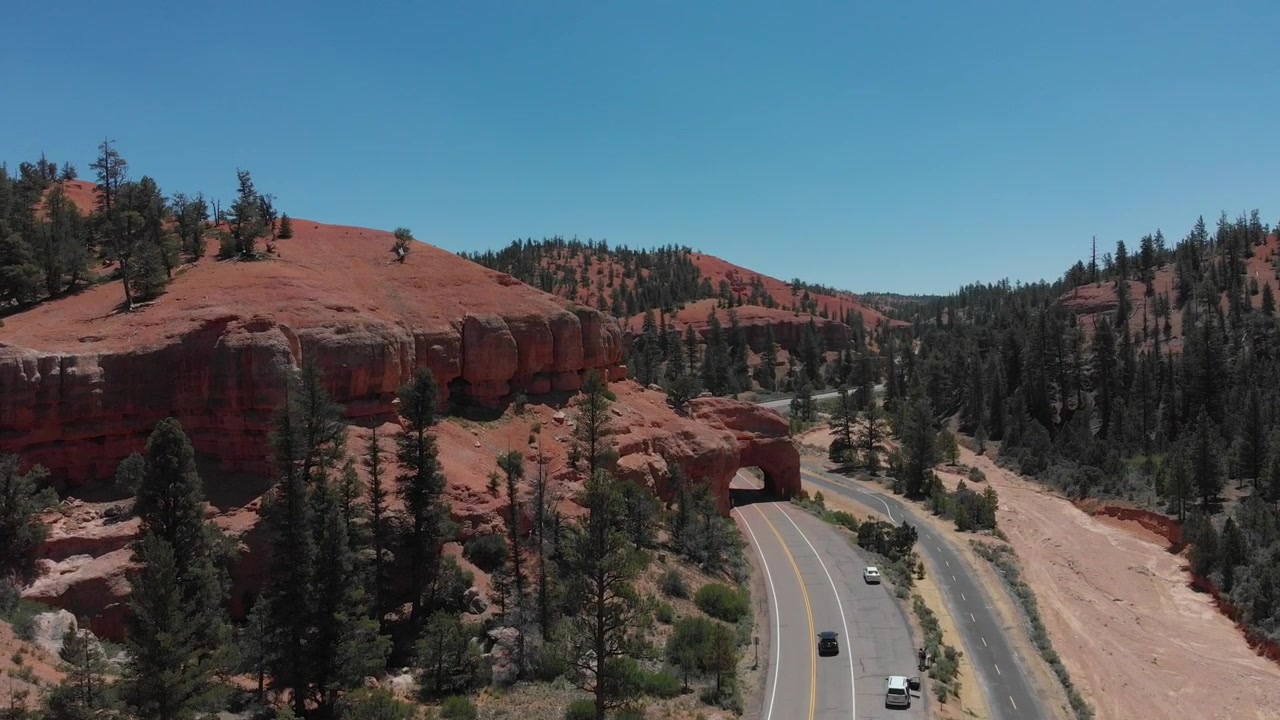 Riprese drone di roccia rossa, con una strada che si snoda tra le colline. Un tunnel e pini sparsi circondano