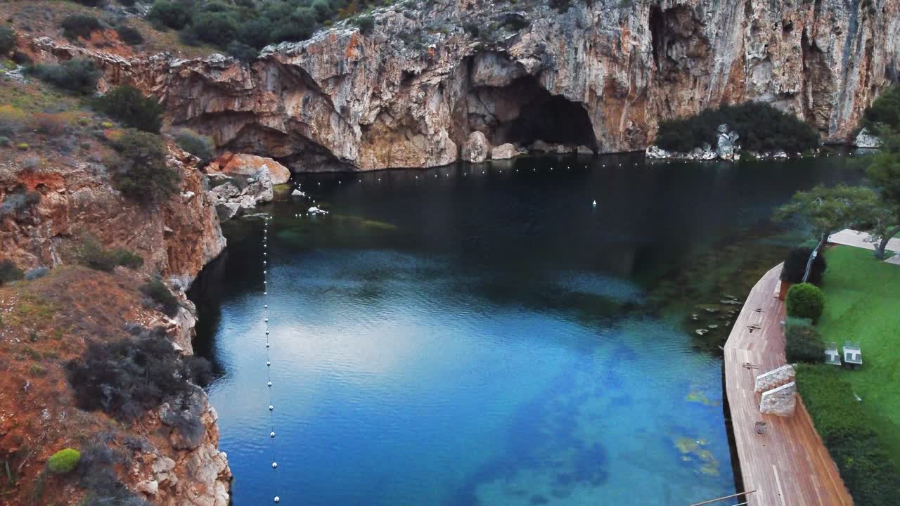 vibrante vista aérea del lago sumergido vouliagmeni en atenas, grecia con los acantilados y cuevas circundantes | 4k