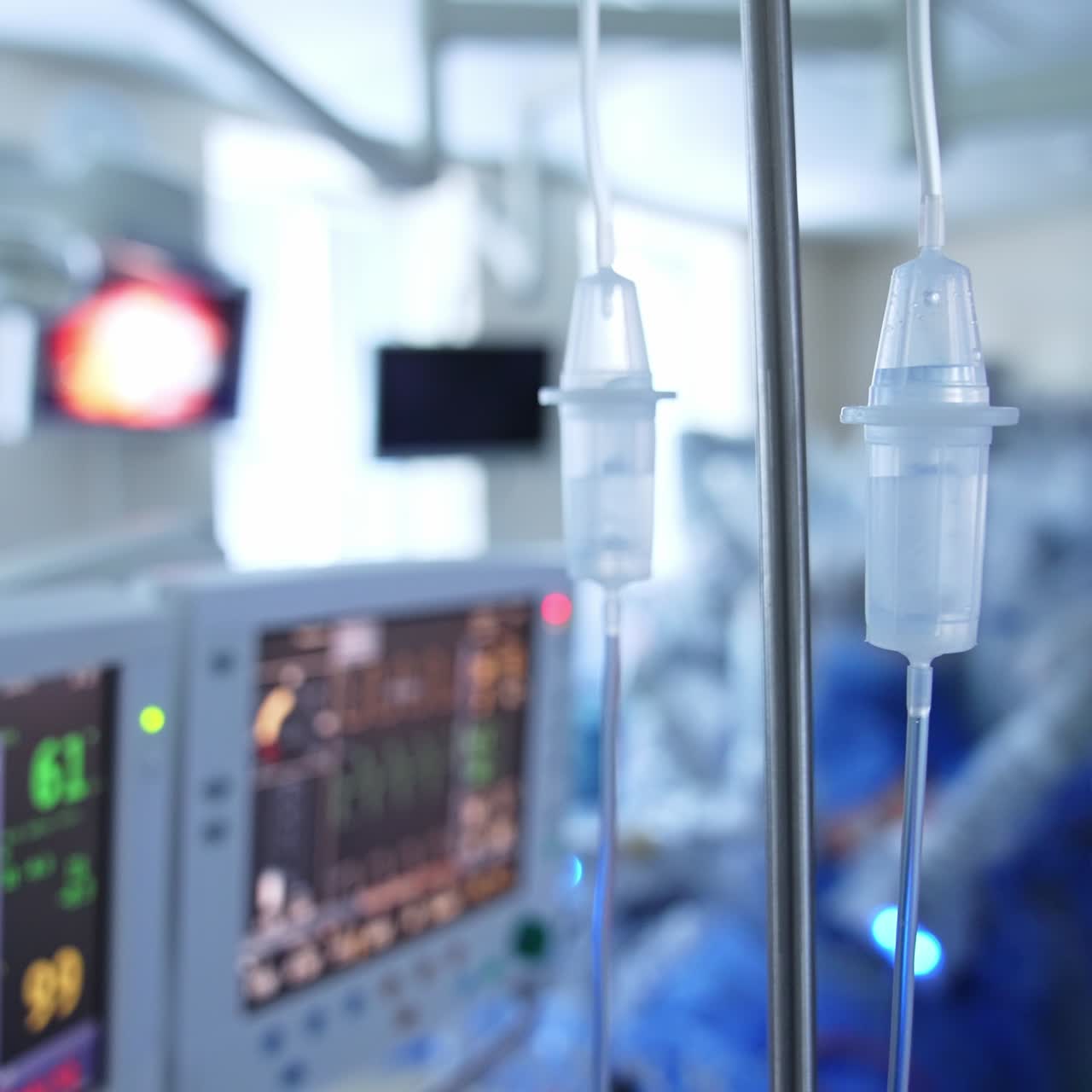 Two drop counters with dripping medicines inside. Screens with patient's vital signs behind in blur. Doctor standing by the robotic machine at backdrop in blur