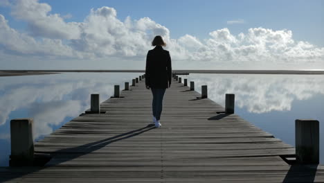woman walking on a pier with cloud reflections in water