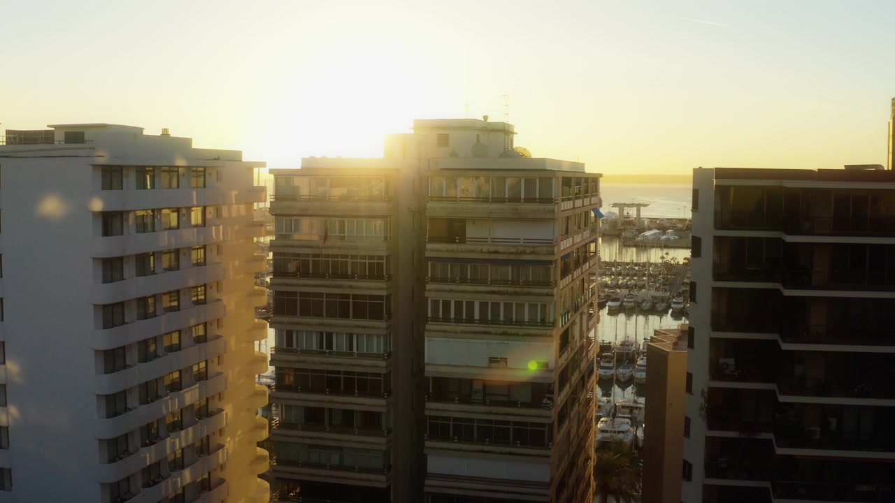 Drone pairando registra o pôr do sol atrás dos edifícios à beira-mar de Palma.