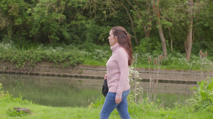 Woman Exercising Outdoors Walking Along Bank Of River With Duck In Background