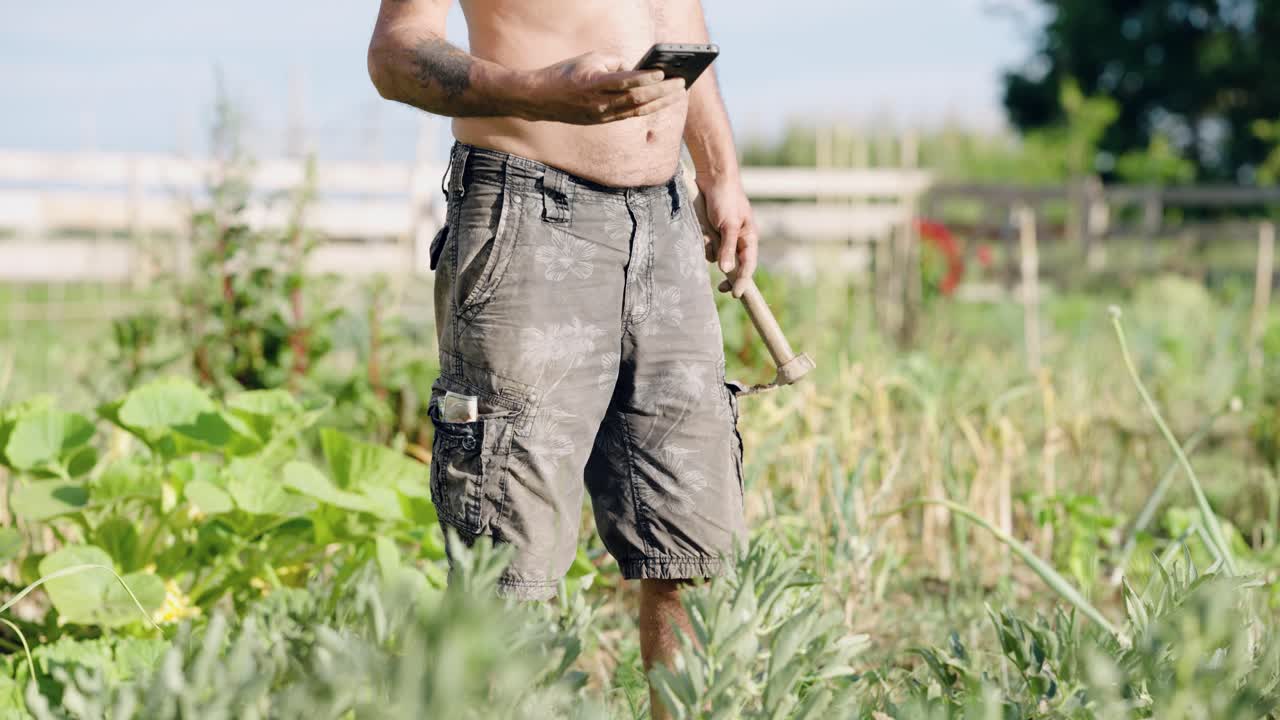 Shirtless farmer using smartphone in vegetable garden