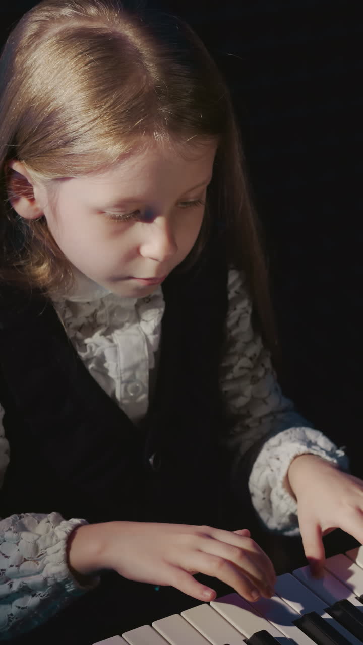 아이는 전기 피아노 키보드에서 간단한 멜로디를 연주합니다. 공식적인 옷을 입은 금발 어린 소녀는 오디오 스튜디오에서 음악적 멜로드를 연주합니다. 음향 콘서트