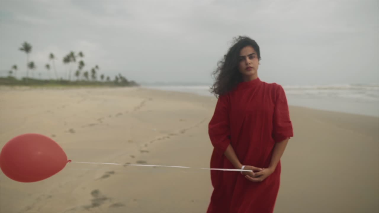 chica india con un globo rojo en la mano con un readdress se encuentra en la playa con el soplo del viento