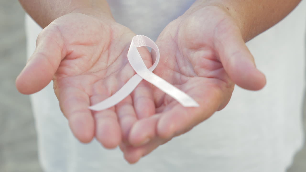 Mani aperte che tengono un nastro per la consapevolezza sul cancro.