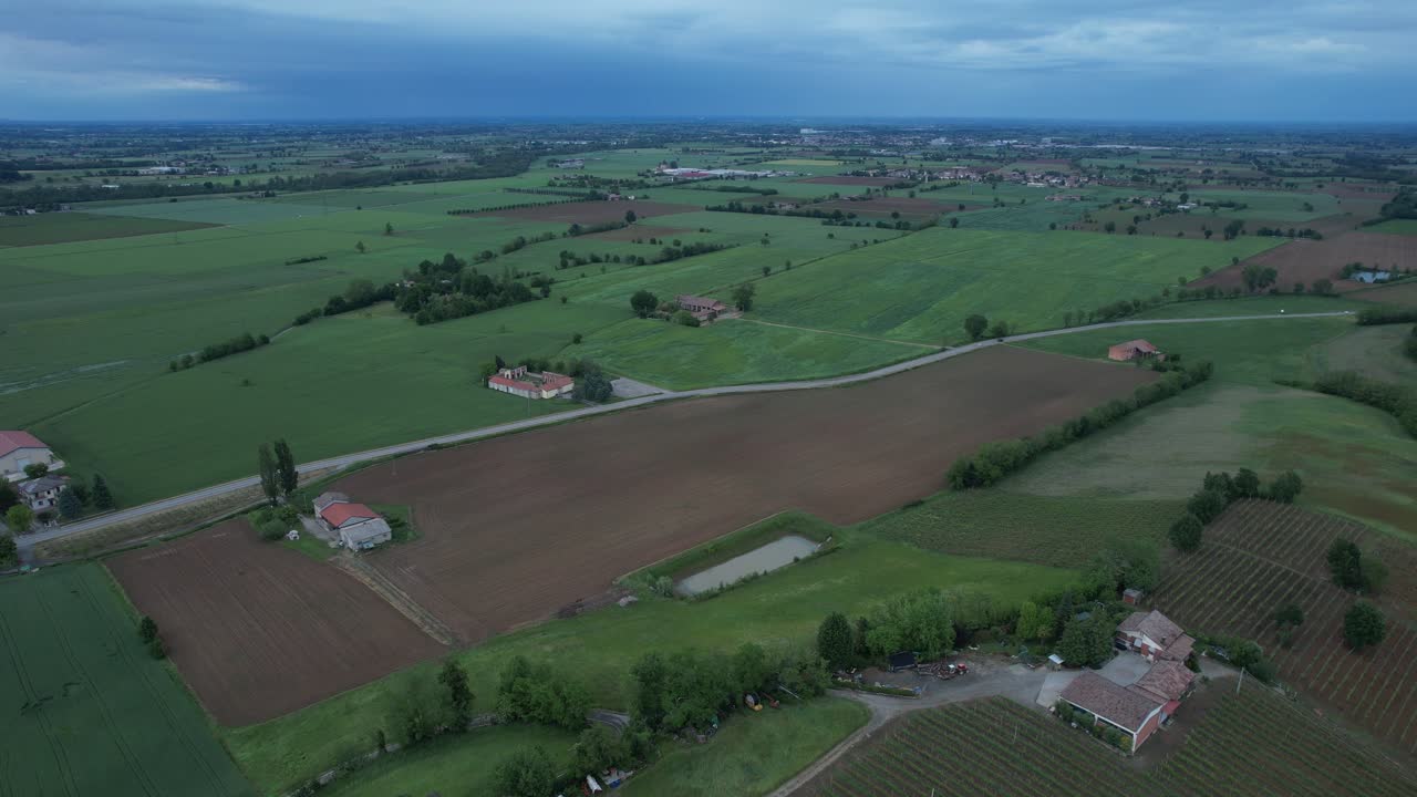 Wide drone establishing shot reveals the rural area of San Lorenzo near Castell’Arquato as cultivated fields, farmhouses, and winding country roads spread across the Po Valley and the nearby Arda Val