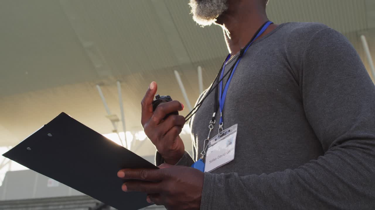Midsection of african american male coach time cheking and making notes