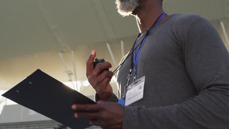 Midsection-of-african-american-male-coach-time-cheking-and-making-notes