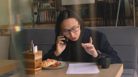 hombre de negocios discutiendo por teléfono celular y revisando algunos documentos mientras almorzaba en una cafetería