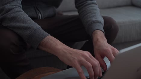 man with slippers sitsc omfortably on couch then types on laptop